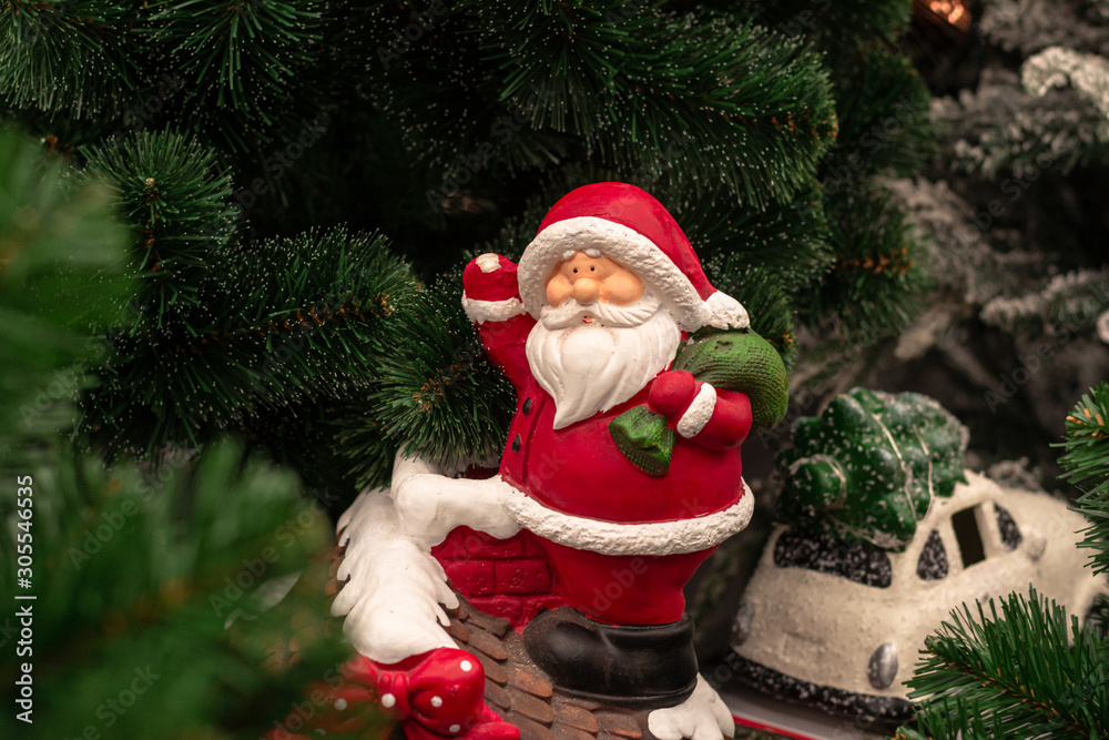 A fragment of a compositional Christmas toy under the Christmas tree, Santa Claus with gifts stands on the roof of the house. The toy symbolizes the New Year.