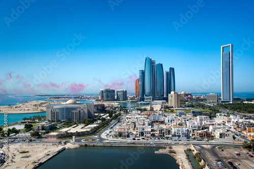 Abu Dhabi skyline with air show colors in the sky and view of the downtown modern buildings