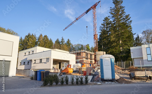 Place of construction of a modern private house using a small crane and a portable toilet for workers on a construction site