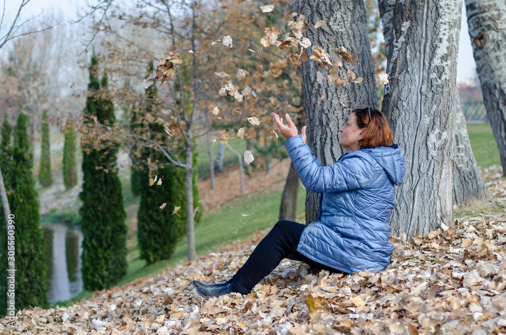 The middle aged woman is playing with autumn leaves