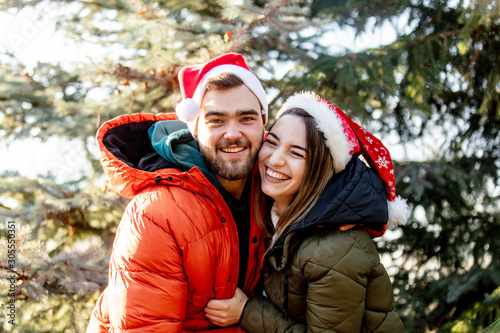 Romantic couple in Christmas hats near fir tree.