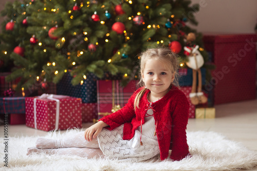 Portrait of a happy pretty girl at the Christmas tree, waiting for the new year
