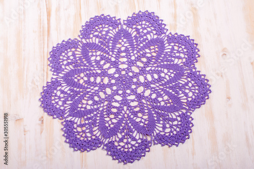 Vintage crocheted round doily with violet pattern on light wooden background. Top view. Decoration of interiors
