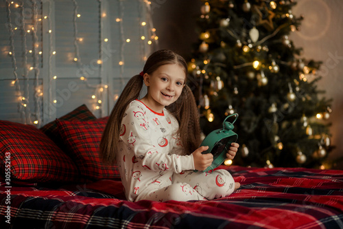 Portrait of a little pretty brunette girl with long beautiful hair on the background of a Christmas tree with lights. Christmas and New Year.