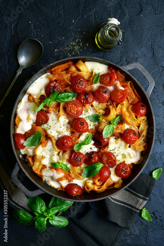 Pasta casserole with tomatoes and mozzarella cheese in a cast iron pan. Top view with copy space.