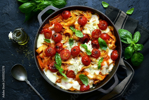 Pasta casserole with tomatoes and mozzarella cheese in a cast iron pan. Top view with copy space. photo