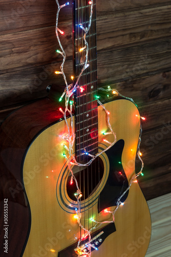 Acoustic guitar in a New Year's garland, guitar in a garland under a wooden wall