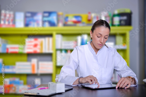 Smiling happy confident young woman pharmacist working on a desk in the pharmacy