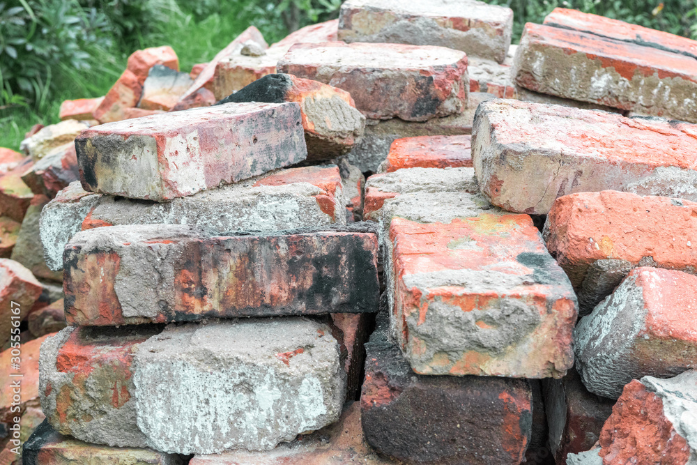 Many old used broken dirty burnt bricks with remnants of cement are stacked in rows on the grass in garden Many old used broken dirty burnt bricks with remnants of cement are stacked in rows on the grass in garden