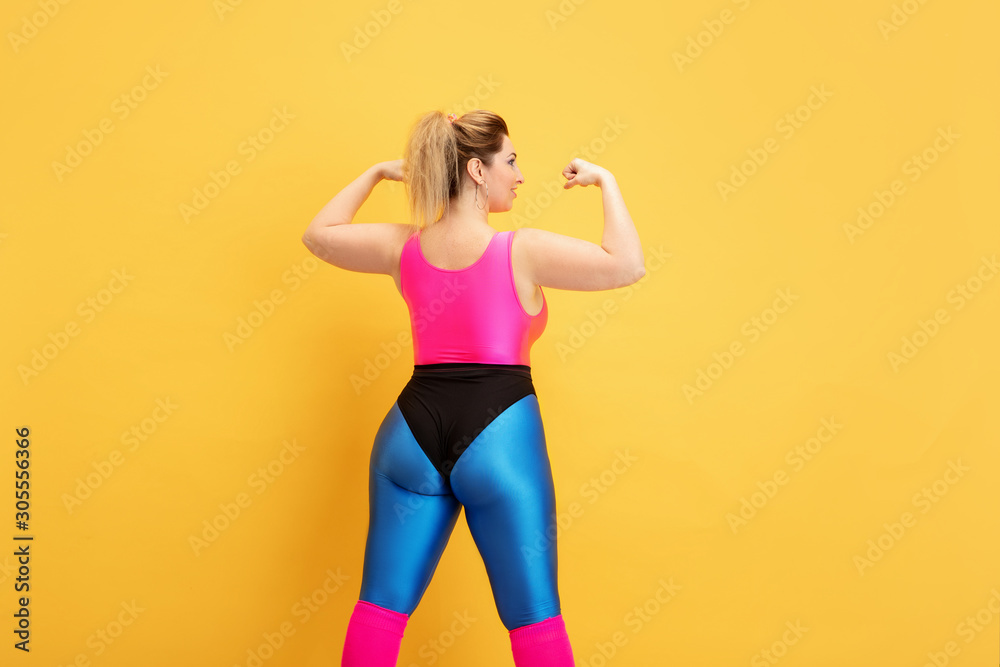 Young caucasian plus size female model's training on yellow background. Copyspace. Concept of sport, healthy lifestyle, body positive, fashion, style. Stylish woman posing confident like superhero. Young caucasian plus size female model's training on yellow background. Copyspace. Concept of sport, healthy lifestyle, body positive, fashion, style. Stylish woman posing confident like superhero.