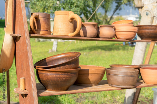 Many clay dishes on wooden shelf in Park. Pottery fair. Potter's craft. Kitchen utensils © Andrey