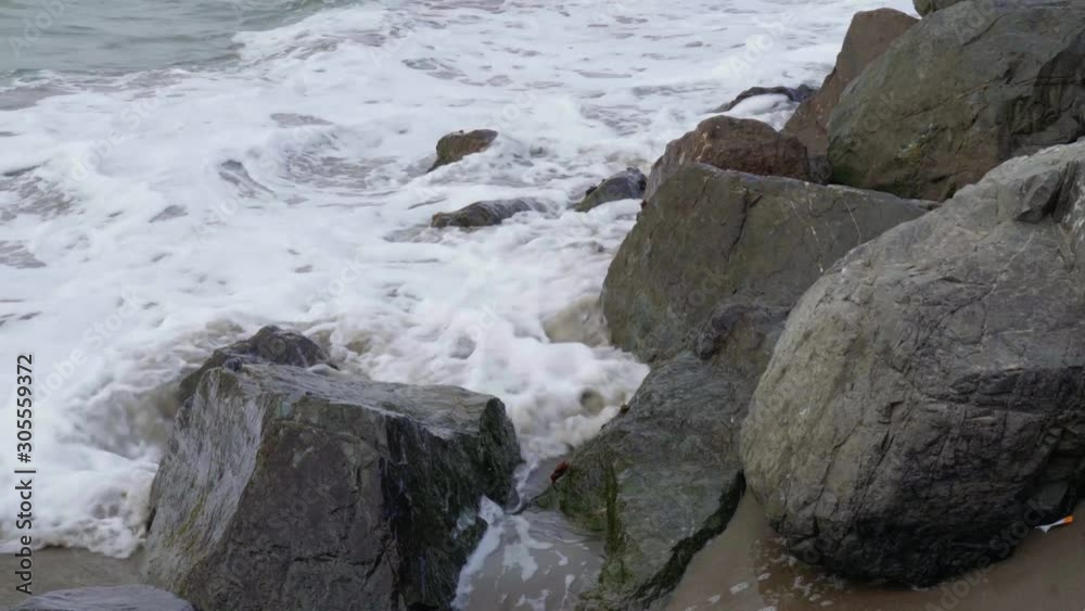 Waves rush onto beach and crash into rocks along the shore. Waves rush onto beach and crash into rocks along the shore.