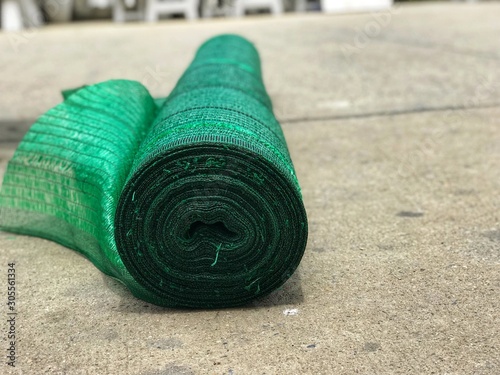 The roll of green shading net is on the concrete floor, it is always used for giving proper climate conditions to the plants.