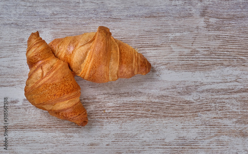 View on two fresh croissants isolated on natural wooden background. Classic French European breakfast. Warm croissants from bakery.