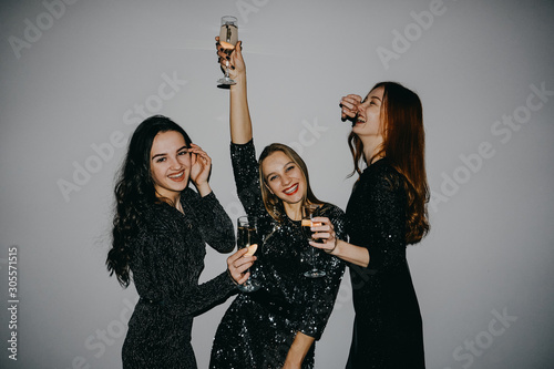 New year celebration party in the club. Three beautiful women in black sparklers night fashion dress singing and dancing with bottle glass of alcohol. Blonde, brunette and redhead celebrate birthday.