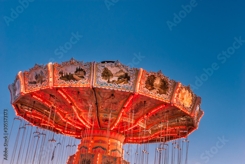 Wall Mural Brightly red lit amusement park twirling swing ride with chains, in a stopped position against a blue hour sky