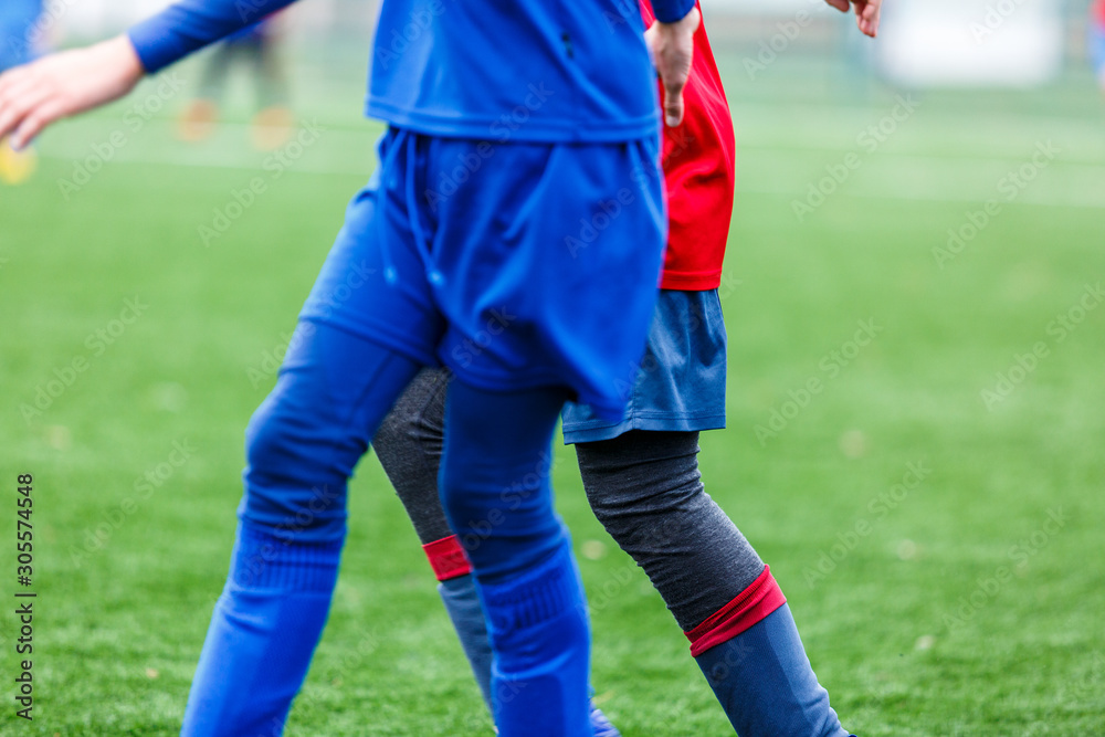 Obraz premium Boys in red and blue sportswear plays football on field, dribbles ball. Young soccer players with ball on green grass. Training, football, active lifestyle for kids concept 