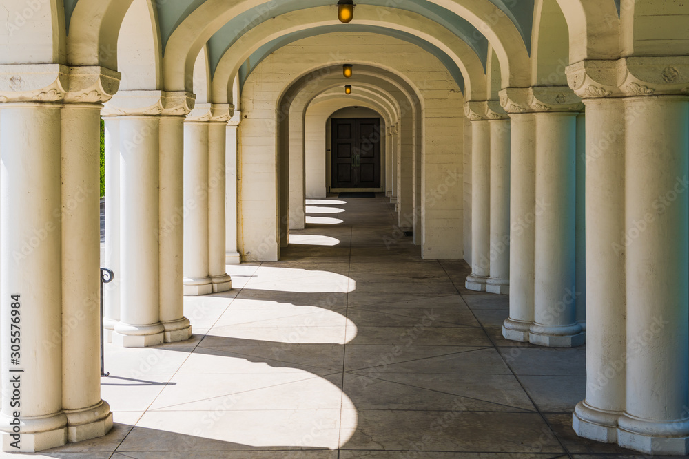 Obraz premium A long corridor in classical architectural style with many elegant columns and arches leading in perspective to a door