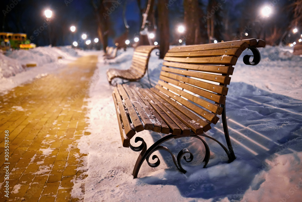 Winter park with benches covered with snow in the evening.
