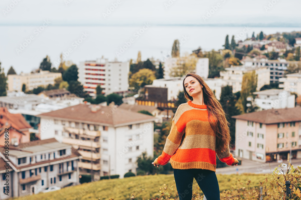 Outdoor portrait of beautiful young woman wearing warm pullover, posing on city background