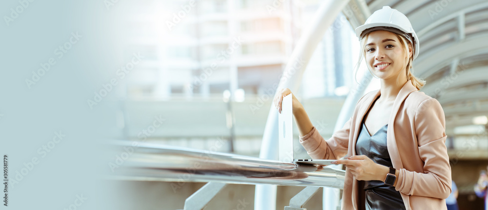 Businesswoman wearing helmet, white construction worker standing, using  laptop to work On job site. Wearing a helmet help to prevent safety and accidents during work. Concept accident insurance - obrazy, fototapety, plakaty 