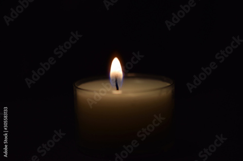 Kerze leuchtet im Dunkeln - kleine weiße Kerze auf schwarzem Hintergrund