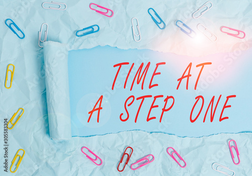 Text sign showing Time At A Step One. Business photo text Slowly but Surely Milestone Careful Gradual Steps Paper clip and torn cardboard placed above a plain pastel table backdrop