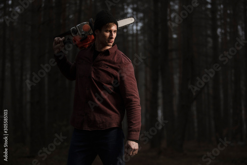 Lumberman working with chainsaw in the forest. Strong lumberjack with the chainsow in the forest.Stylish lumberman getting ready for work. Lifestyle. photo