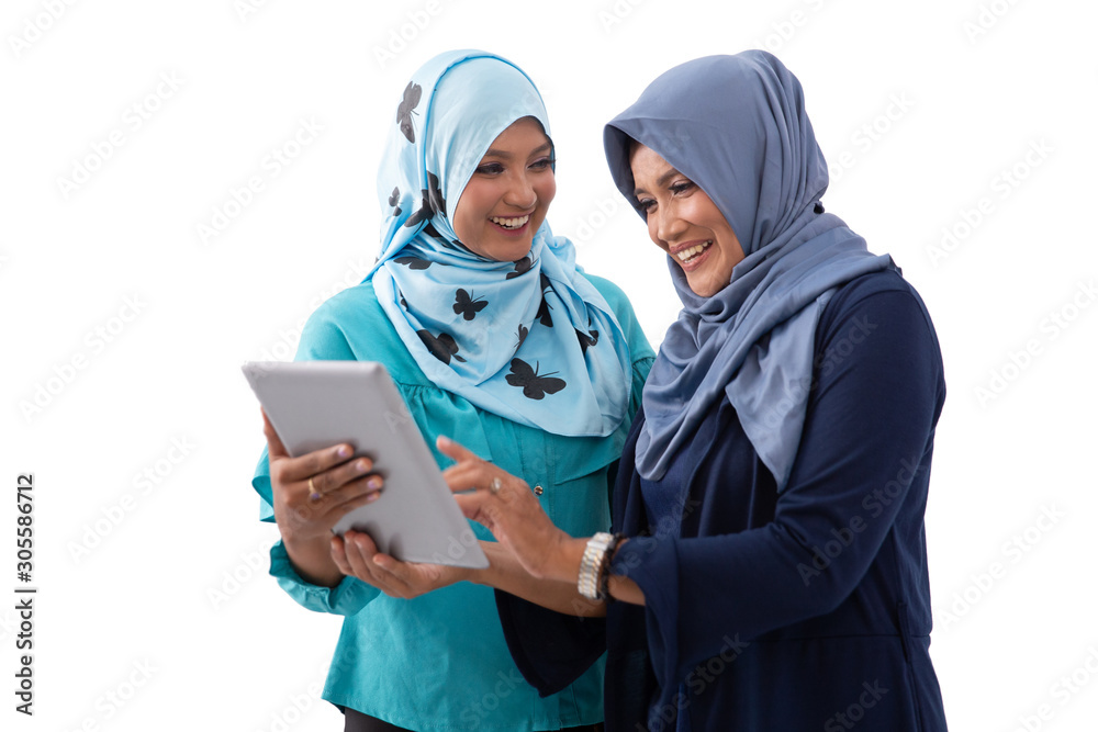 Portrait of veiled young woman showing a tablet to her mother while laughing happily in an isolated background Portrait of veiled young woman showing a tablet to her mother while laughing happily in an isolated background