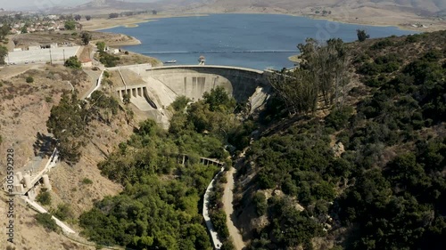 Nice slow and low push in and flyover huge concrete historic dam with reservoir and mountains behind it, white birds in background on water photo