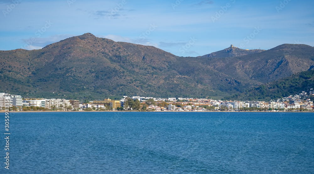 Seascape in Roses, Catalonia, Spain. City on the mountain on the coast on blue sky background. Beautiful panoramic view in the sunny day, natural background. The bay and the city in the Mediterranean.