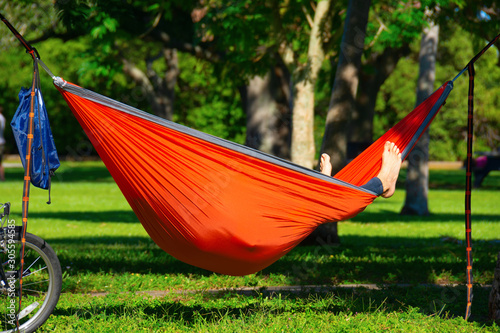 A man enjoying a beautiful sunny afternoon hanging out relaxing in his hammock in a park with trees in the background