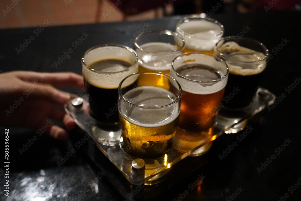 Close up of craft beer tasting flight at local brewery of small pint glasses in a row on a tray with rainbow variety of dark malt stouts to golden yellow hoppy ales on Close up of craft beer tasting flight at local brewery of small pint glasses in a row on a tray with rainbow variety of dark malt stouts to golden yellow hoppy ales on
