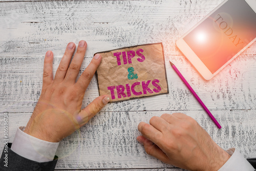 Text sign showing Tips And Tricks. Business photo text Steps Lifehacks Handy advice Recommendations Skills Hand hold note paper near writing equipment and modern smartphone device photo