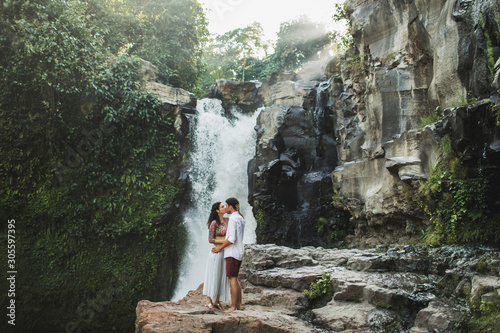 Young couple in love kissing with amazing view of Tegenungan cascade waterfall. Happy together, honeymoon in Bali. Travel lifestyle. photo