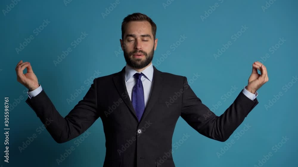 Calm businessman in campaign suit relaxing, meditating. Handsome european man calms down, breathes deeply with mudra om. Slow motion. Studio footage.