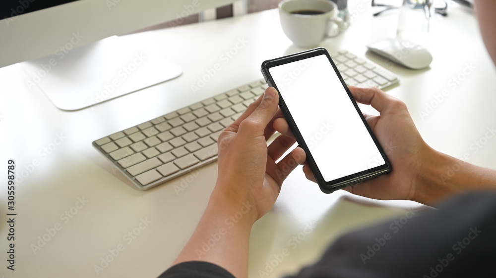 Cropped shot young man holding empty screen of mobile phone on office desk. Cropped shot young man holding empty screen of mobile phone on office desk.