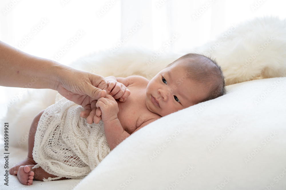 Young asian woman mother hand holding adorable newborn baby girl infant hand that relax resting in white baby sleeper with love. Baby looking at mother. Maternity and newborn baby health care concept. Young asian woman mother hand holding adorable newborn baby girl infant hand that relax resting in white baby sleeper with love. Baby looking at mother. Maternity and newborn baby health care concept.