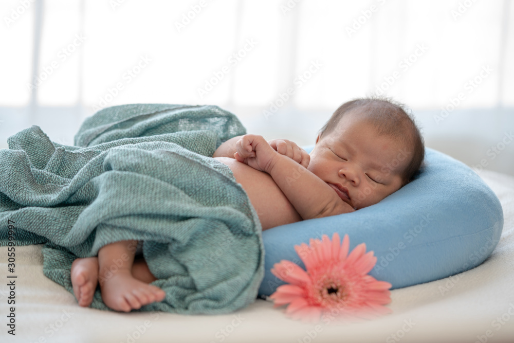 Beautiful skinny asian newborn baby girl infant sleeping on blue baby  sleeper. Relaxing adorable newborn baby daughter lying down on the bed.  Maternity and newborn baby health care insurance concept. Stock Photo