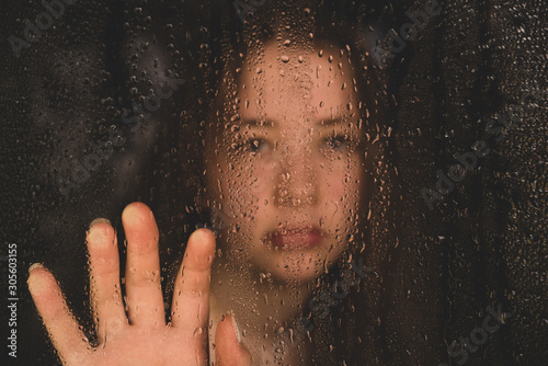 Teenage girl with hand on window in the rain
