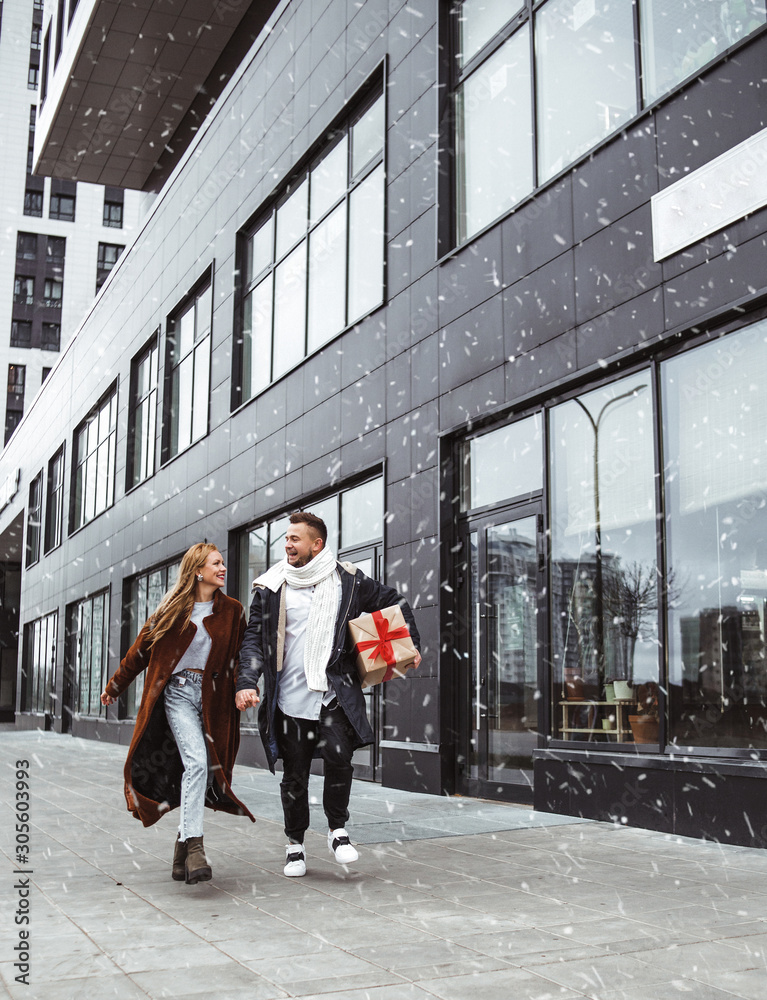 Happy laughing winter  young couple walking in the street with Christmas gifts presents in snowy weather. Christmas and holiday concept