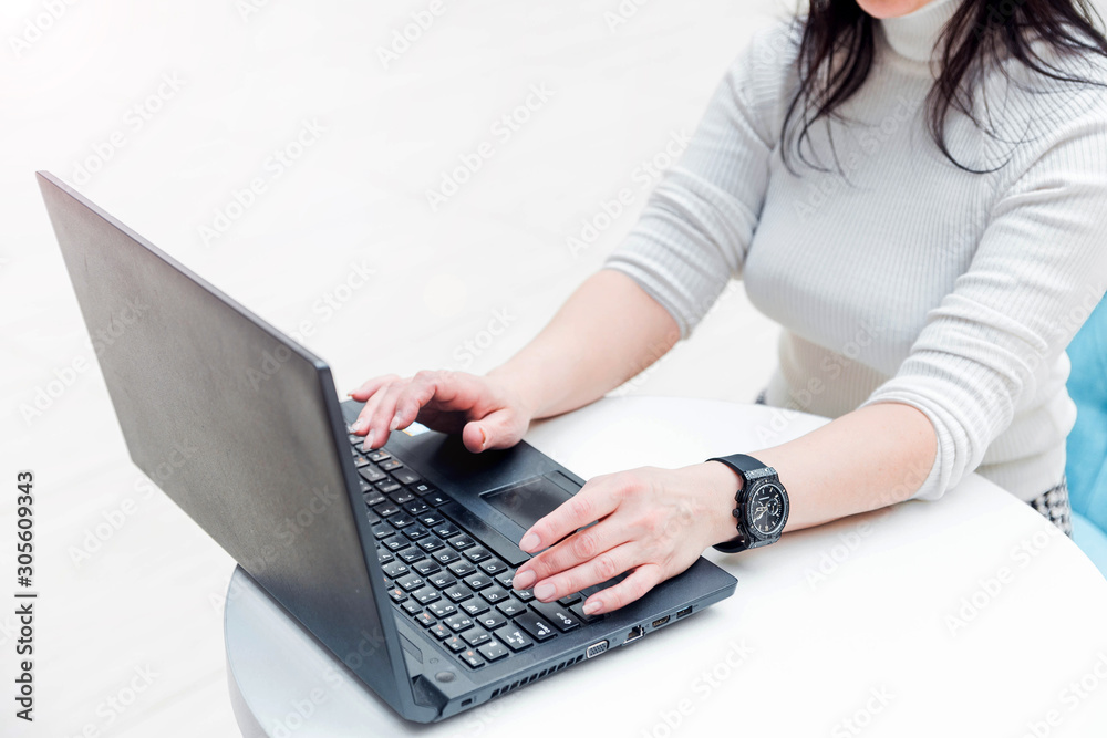 Naklejka premium Stylish woman in a white sweater sits at a white table and works at a laptop