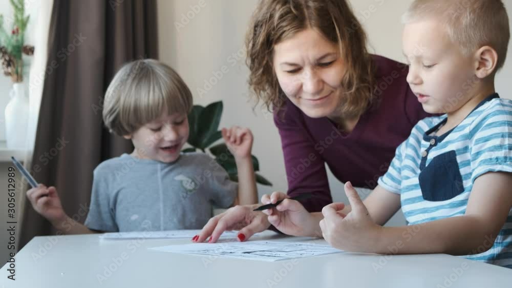 Two little boys sitting at the table at home and drawing together with their mom. Family concept Two little boys sitting at the table at home and drawing together with their mom. Family concept