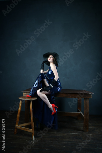 girl in a blue evening dress and in a black hat on a gray background