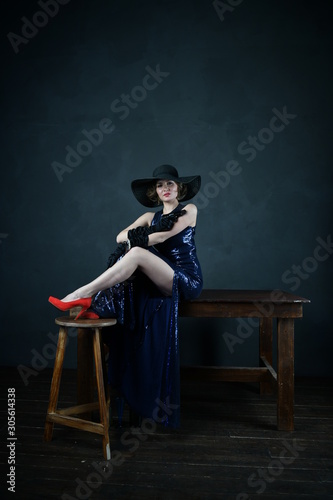 girl in a blue evening dress and in a black hat on a gray background with a gun