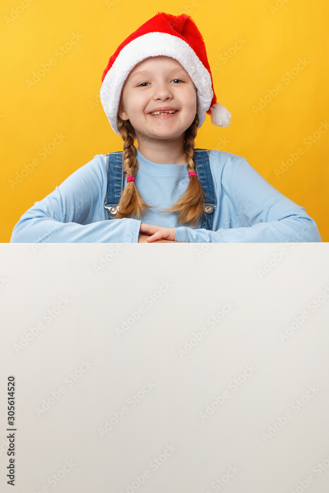 Happy child in santa hat is holding a blank space banner on a yellow background. Christmas card Happy child in santa hat is holding a blank space banner on a yellow background. Christmas card