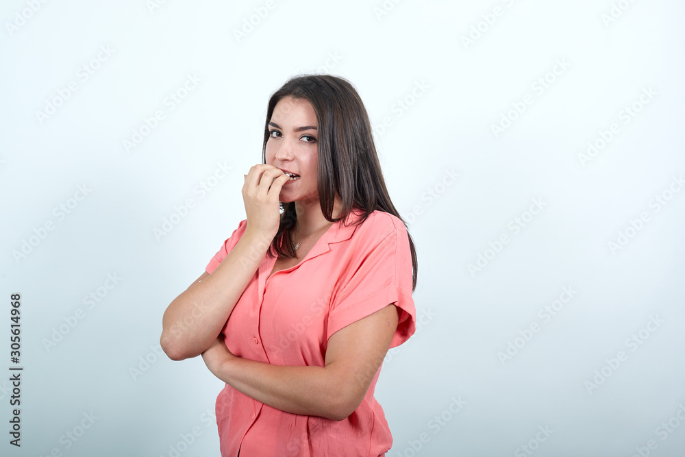 Nervous caucasian young woman in pink shirt isolated on white background in studio, biting his nails, worried about something . People sincere emotions, lifestyle concept. Nervous caucasian young woman in pink shirt isolated on white background in studio, biting his nails, worried about something . People sincere emotions, lifestyle concept.