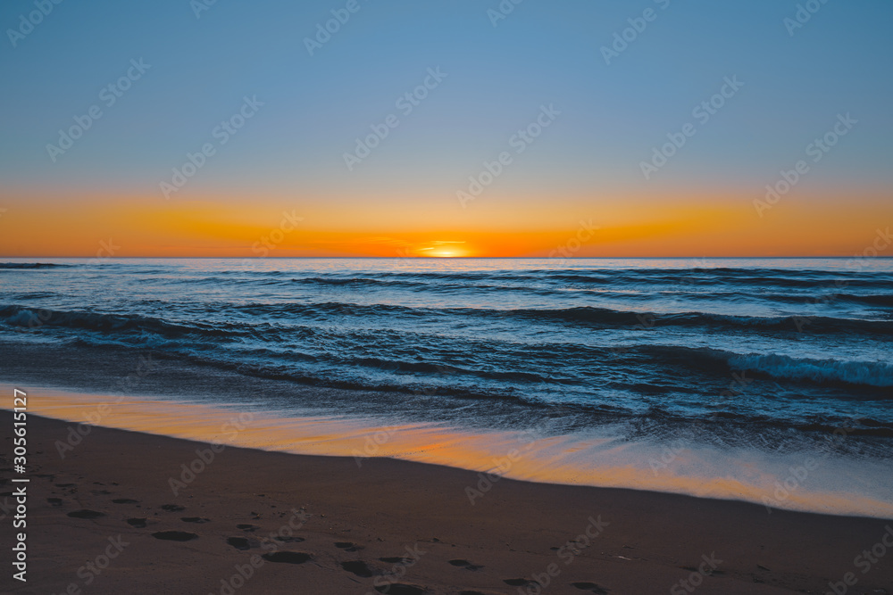 Abstract seascape. Beautiful tropical beach at sunset. Blue ocean, colorful sky, and sun setting down the horizon