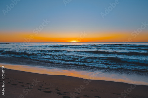 Abstract seascape. Beautiful tropical beach at sunset. Blue ocean, colorful sky, and sun setting down the horizon