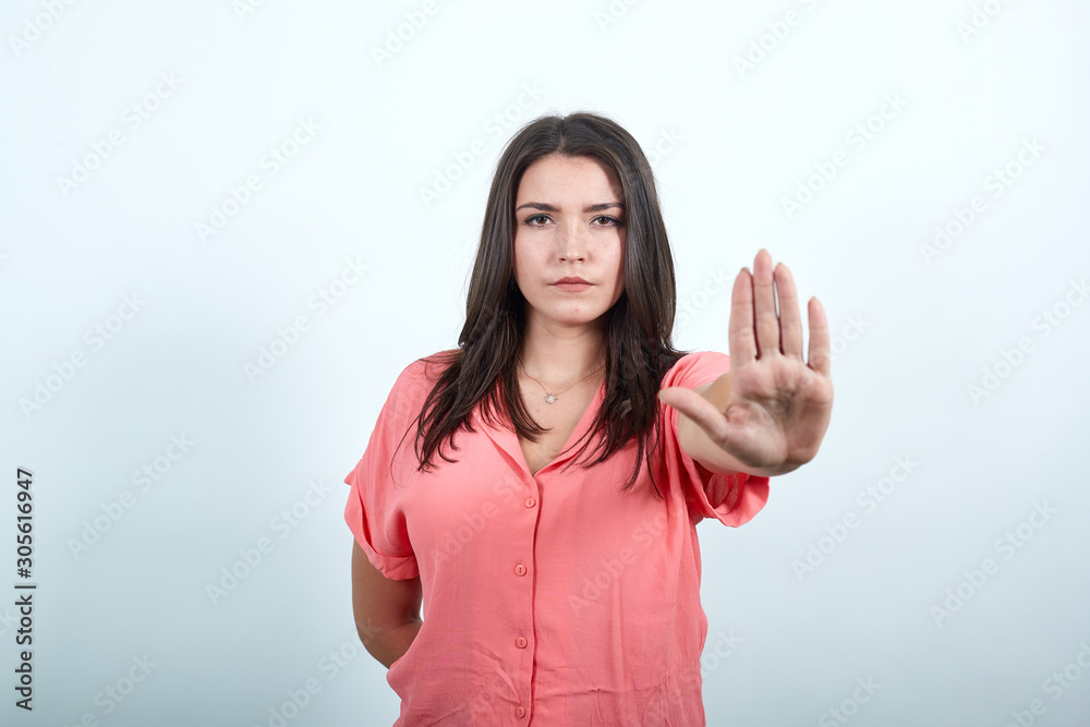 Attractive caucasian young woman in pink shirt doing No, stop gesture isolated on white background in studio. People sincere emotions, lifestyle concept.